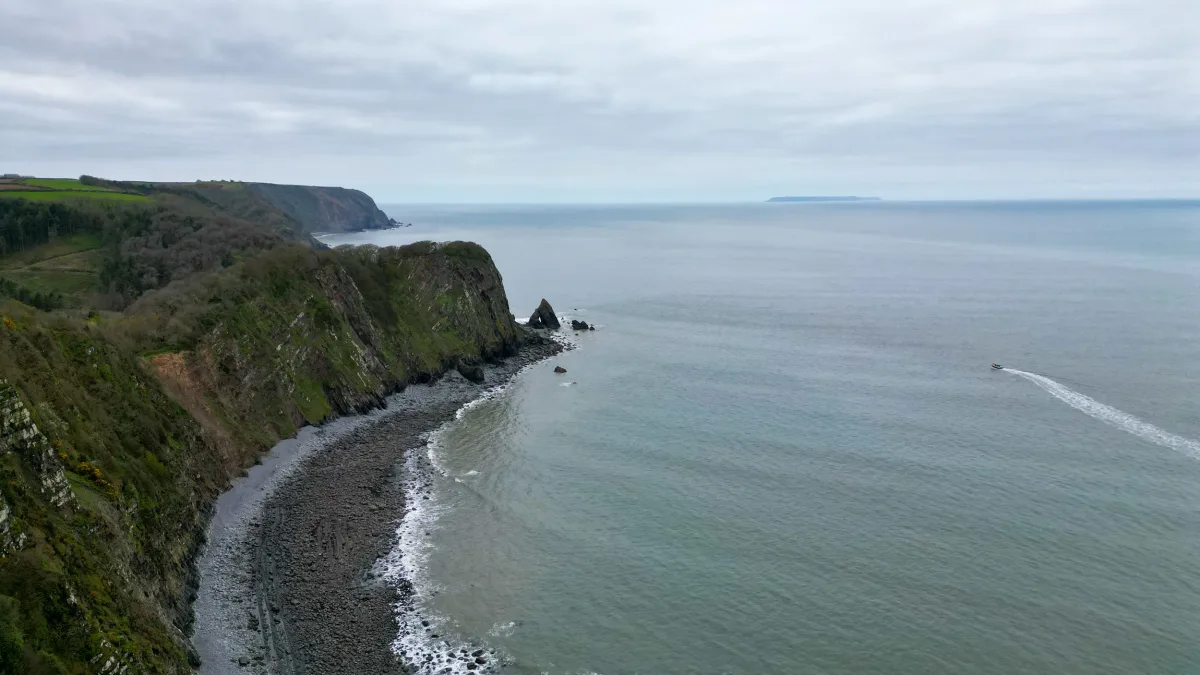 Aerial of the rugged North Devon coast, a workboat leaving a wake out to sea